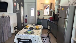A compact kitchen with a dining table set for four, a refrigerator, and a small window. - Le gîte des Toussillards (TOUSSIEU)