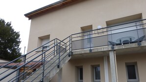 A building with a beige exterior, a metal staircase with railings, and a car parked in front. - Le gîte des Toussillards (TOUSSIEU)