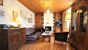 Ein traditionell eingerichteter Raum mit Holzboden, einer Couch, einem Sessel, einem Tisch und einem Kamin.