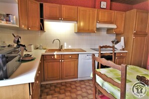 Une cuisine avec des meubles en bois, un plan de travail blanc, un évier, un lave-vaisselle et une chaise avec une table.