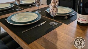 Et spiseområde med et bord dækket til fire personer, en vinflaske og et køkken i baggrunden.