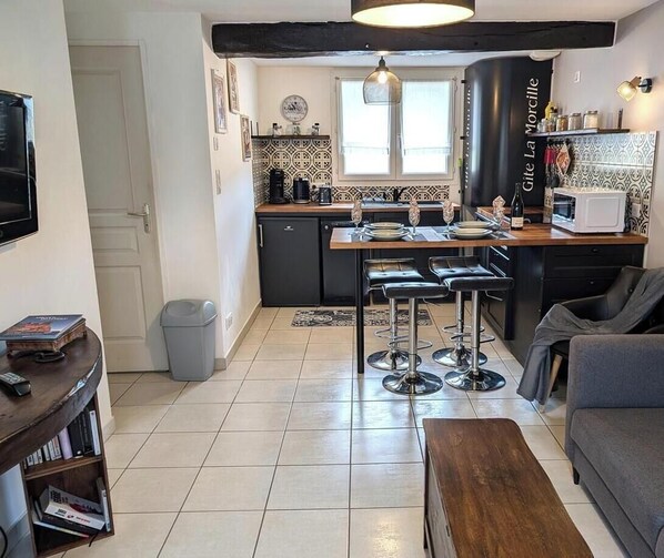 Eine kompakte Küche mit Essbereich, ein graues Sofa und ein Fernseher in der Ecke.
