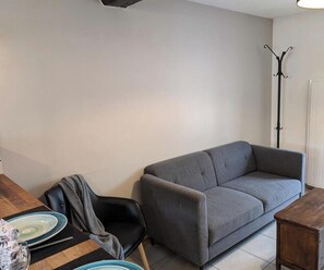 Ein Wohnzimmer mit grauem Sofa, einem Holztisch mit Tellern und einem Kleiderständer an der Wand.