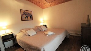 Una camera da letto con soffitto in legno, un letto con biancheria bianca, due abat-jour e un quadro con un elefante appeso al muro.