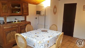 Un'area pranzo con un tavolo ricoperto da una tovaglia fantasia, circondato da sedie in vimini. Sopra il tavolo è montato un forno a microonde, e si nota un termosifone bianco sulla parete.