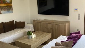 Ein modernes Wohnzimmer mit einer Sofagarnitur, einem Couchtisch, einem Fernseher und einer Klimaanlage.