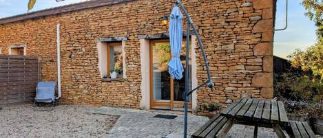 A stone building with a wooden door, a small window, and a patio area with a bench and a table.