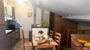A dining area with a wooden table set for four, surrounded by chairs. There is a kitchen area with modern appliances and a coffee machine. A sofa and a plant are visible in the background. - La Cadole - CHARNAY - Gîte (CHARNAY)