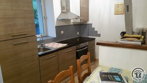 A compact kitchen with wooden cabinets, a stainless steel range hood, a black countertop, and a dining area with a table set for two. - La Cadole - CHARNAY - Gîte (CHARNAY)