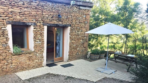 A stone building with two windows and a door, a patio with a table and chairs, and a white umbrella. - La Cadole - CHARNAY - Gîte (CHARNAY)