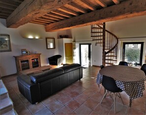 Uma sala de estar espaçosa com teto de madeira, um sofá de couro preto, uma mesa de jantar com toalha listrada e uma escada em espiral.