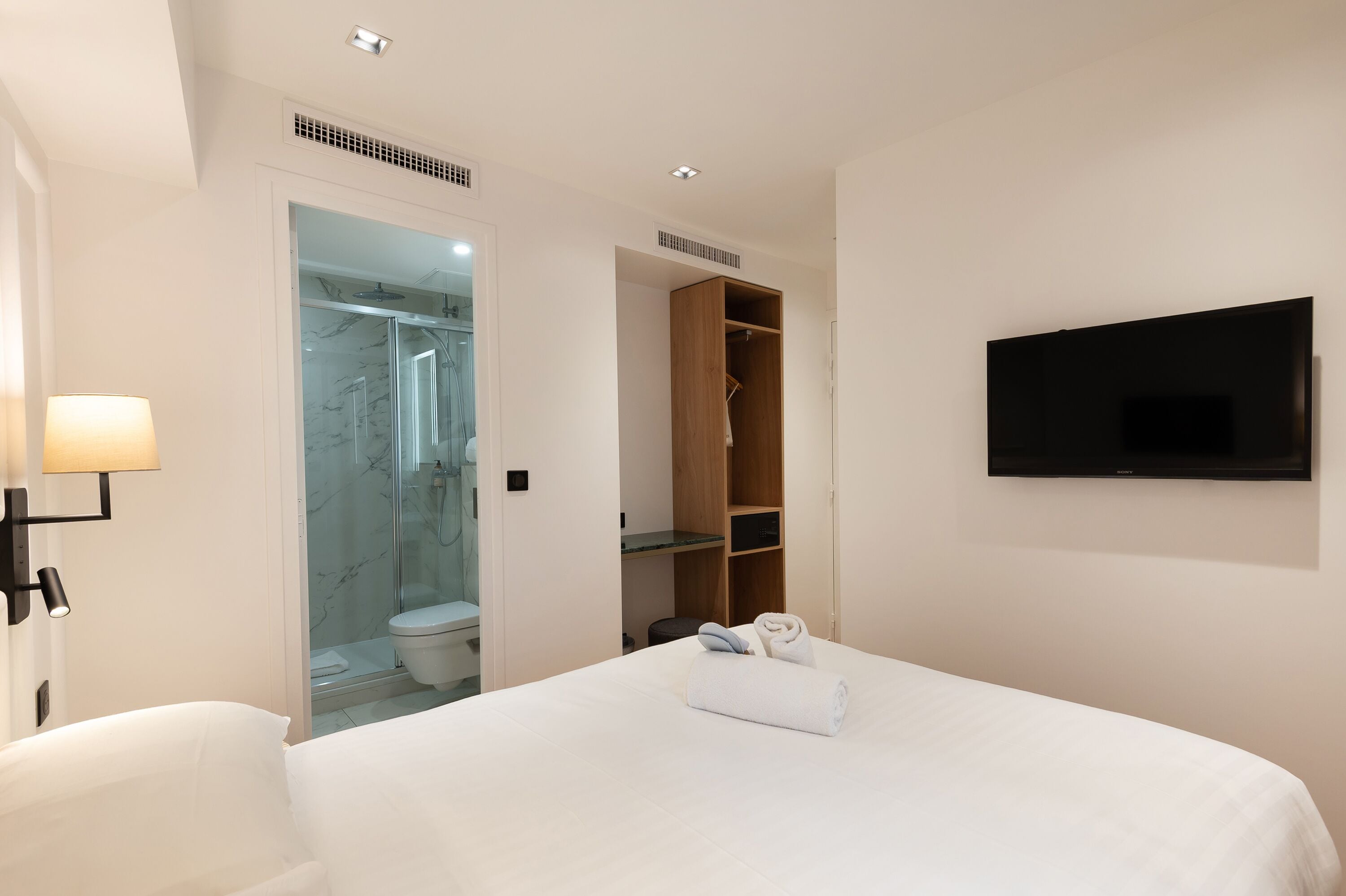 Hotelkamer met een bed, een aan de muur bevestigde televisie, een inloopkast en een douchehoek.