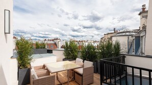 A rooftop terrace with a table and chairs, surrounded by potted plants, overlooking a cityscape. - Hotel au Coeur de Republique (Paris)
