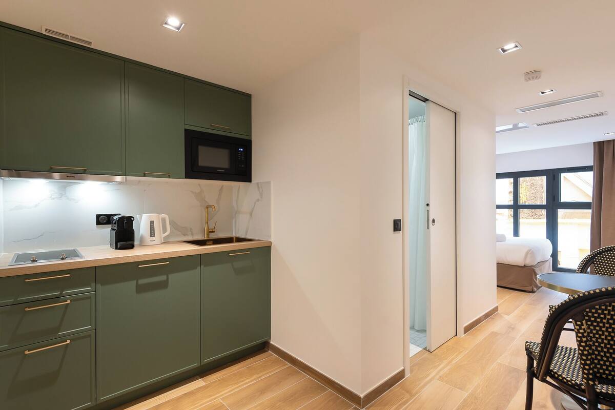 A modern kitchen with green cabinets, a microwave, and a coffee maker.