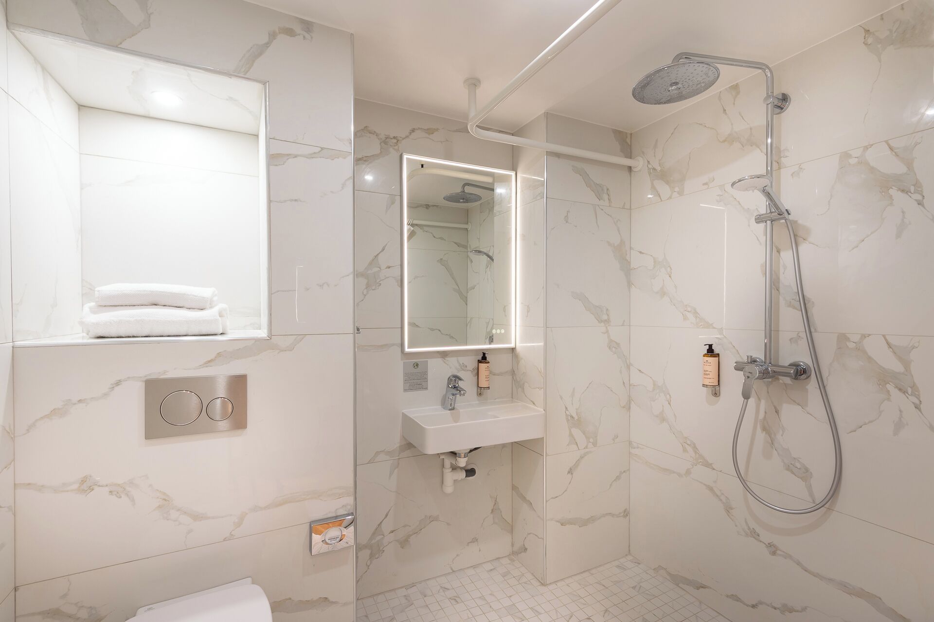 A modern bathroom with a marble floor, a built-in sink, a mirror, and a shower with a handheld showerhead.