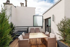 A rooftop terrace with a glass door, wicker furniture, and a view of the sky. - Hotel au Coeur de Republique (Paris)