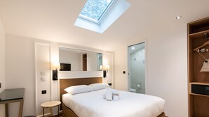A hotel room with a skylight, a bed with white linens, a bedside table, a mirror, and a wardrobe. - Hotel au Coeur de Republique (Paris)