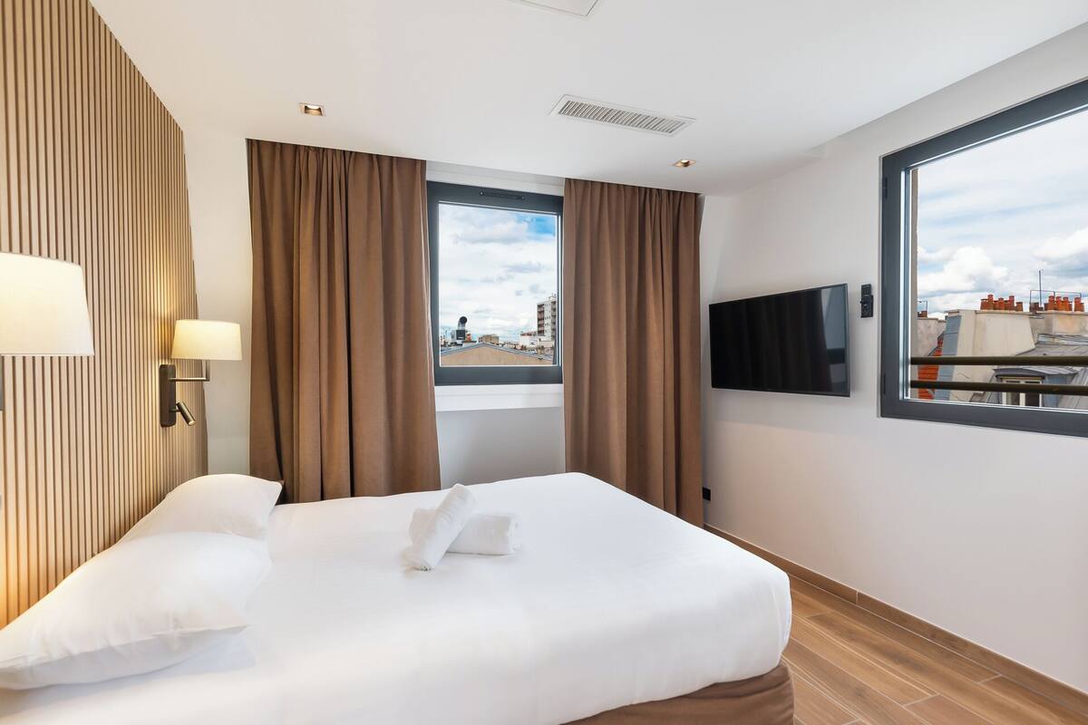 A hotel room with a bed, a TV, and a window with curtains.