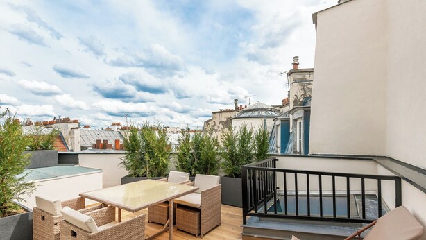 A rooftop terrace with wicker furniture, a glass table, and a view of the cityscape. - Hotel au Coeur de Republique (Paris)