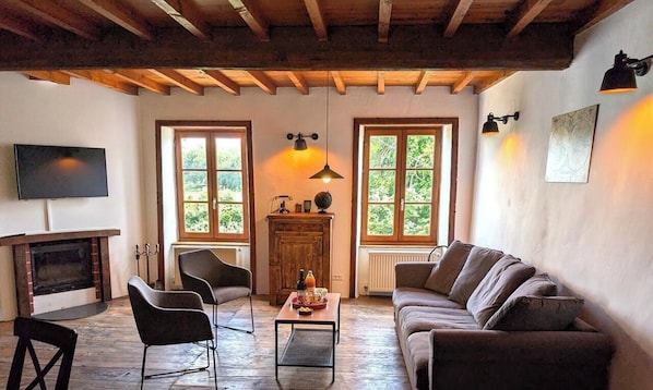 A cozy living room with a fireplace, wooden beams, a sofa, chairs, and a television.