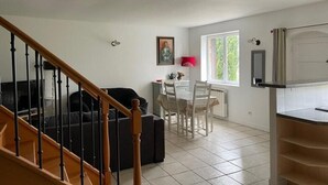 A spacious living area with a staircase, a dining table with chairs, and a kitchen area with a window. - La Colombière - SAINT-SYMPHORIEN-D'OZON (Saint-Symphorien-d'Ozon)
