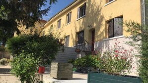 A yellow building with a staircase leading to a door. There are potted plants and a bench in the foreground. - La Colombière - SAINT-SYMPHORIEN-D'OZON (Saint-Symphorien-d'Ozon)