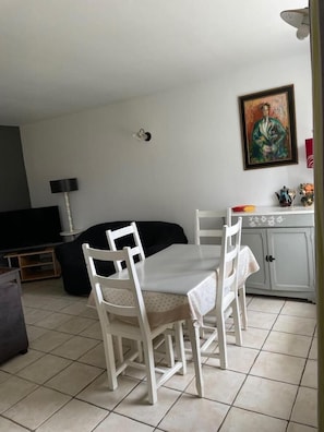 A dining area with a table and chairs, a sofa, a TV, a lamp, and a painting on the wall. - La Colombière - SAINT-SYMPHORIEN-D'OZON (SAINT-SYMPHORIEN-D'OZON)