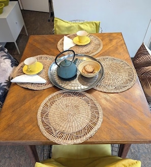 A wooden dining table with woven placemats, yellow cups, a teapot, and a plate with cookies. - La Petite Maison - TASSIN LA DEMI LUNE (TASSIN LA DEMI LUNE)
