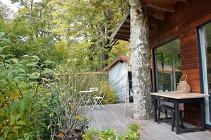 Een houten terras met een tafel en stoelen, omringd door planten en bomen.