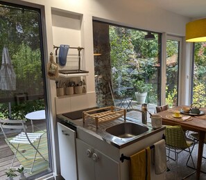 Una cocina moderna con un lavamanos integrado, un escurreplatos de madera y un comedor con una mesa dispuesta para dos personas.
