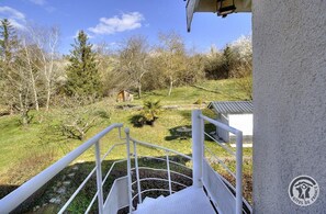 Un escalier menant à un balcon qui donne sur un espace verdoyant, avec des arbres et un petit bâtiment.