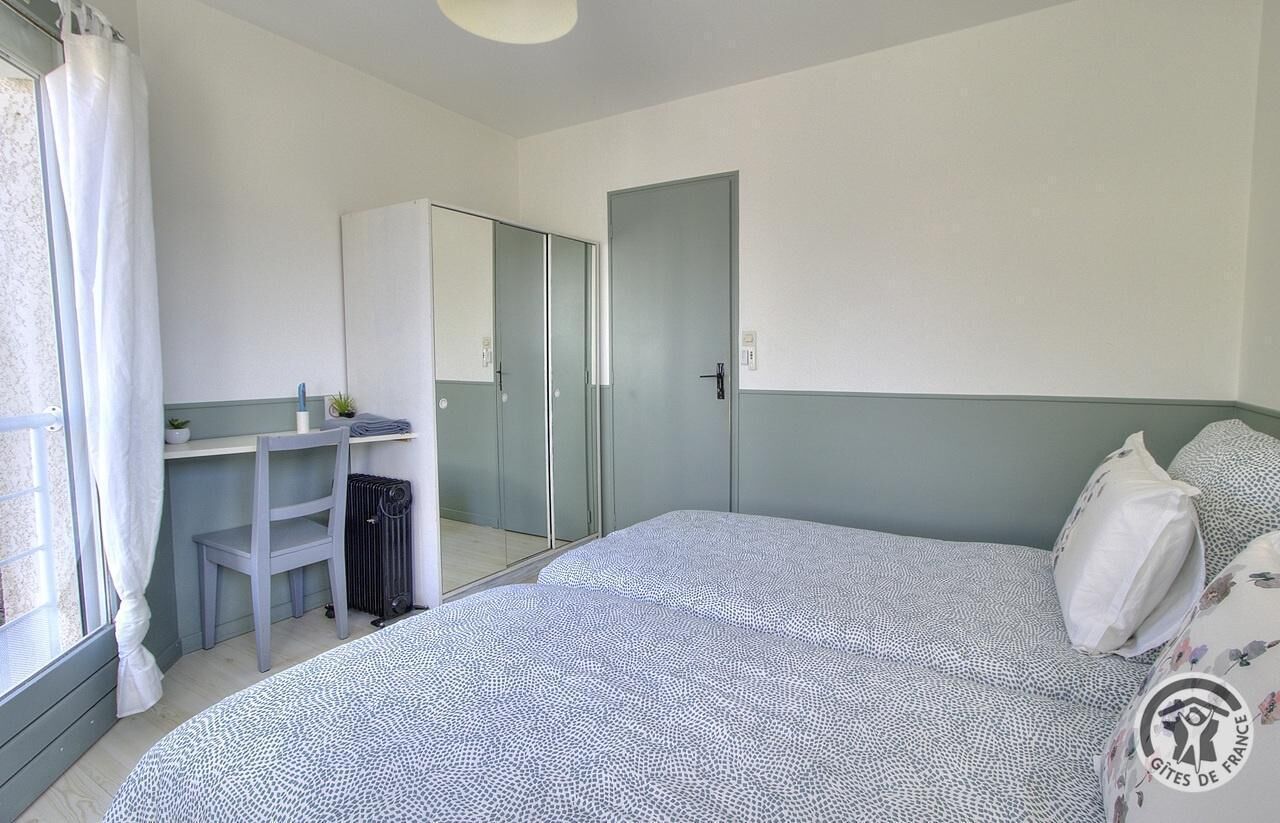 A bedroom with a bed, a desk, a chair, a radiator, and a wardrobe.