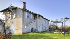 Una casa de dos pisos con un patio, una pérgola y una mesa de picnic.