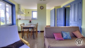 Una habitación acogedora con una mesa de comedor dispuesta para dos personas, un sofá con cojines y una ventana con cortinas.