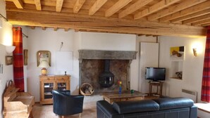 A cozy living room with a fireplace, wooden beams, a sofa, a television, and a piano.