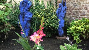 Two statues in a garden with a brick wall background.