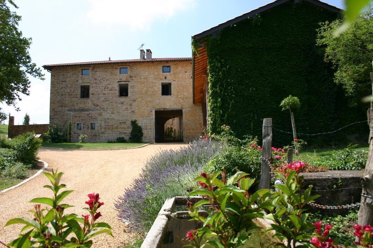 Un bâtiment en pierre avec une porte en bois et un jardin agrémenté de fleurs et d’un petit étang.