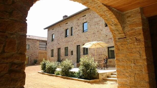 A courtyard with a stone archway, a brick building, and a table with an umbrella.