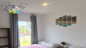 A room with two beds, a window with curtains, a wall with photos, and a small table with a vase. - Flat1 Complete 5 minutes from the Taipu de Fora Swimming Pools (Marau)