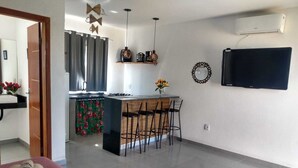 A modern kitchen with a central island, bar stools, and a flat-screen TV mounted on the wall. - Flat1 Complete 5 minutes from the Taipu de Fora Swimming Pools (Marau)