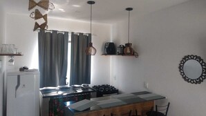 A compact kitchen with a central island, two hanging pendant lights, and a refrigerator. - Flat1 Complete 5 minutes from the Taipu de Fora Swimming Pools (Marau)