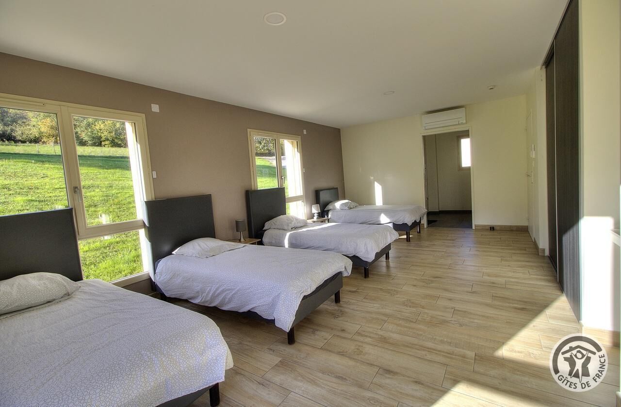 Ein Hotelzimmer mit vier nebeneinander stehenden Betten, großen Fenstern und Blick auf eine grüne Landschaft.
