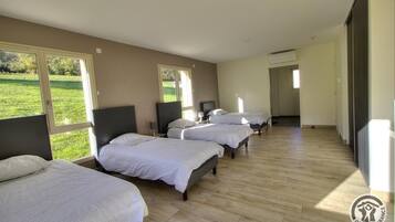 Ein Hotelzimmer mit vier nebeneinander stehenden Betten, großen Fenstern und Blick auf eine grüne Landschaft.