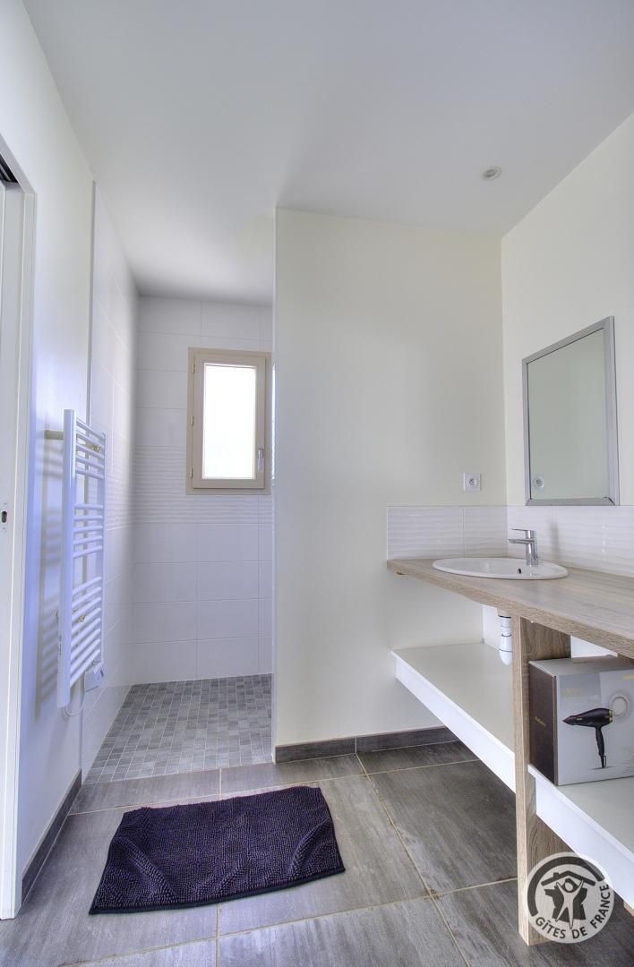 A modern bathroom with a white sink, a mirror, and a window.