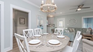 A dining area with a round table set for six, surrounded by white chairs. - The Rookery Iii 6015 3 Bedroom Cottage by RedAwning (Gulf Shores)