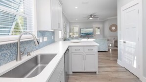 A modern kitchen with white cabinetry, a large island, and a view of the living area. - The Rookery Iii 6015 3 Bedroom Cottage by RedAwning (Gulf Shores)