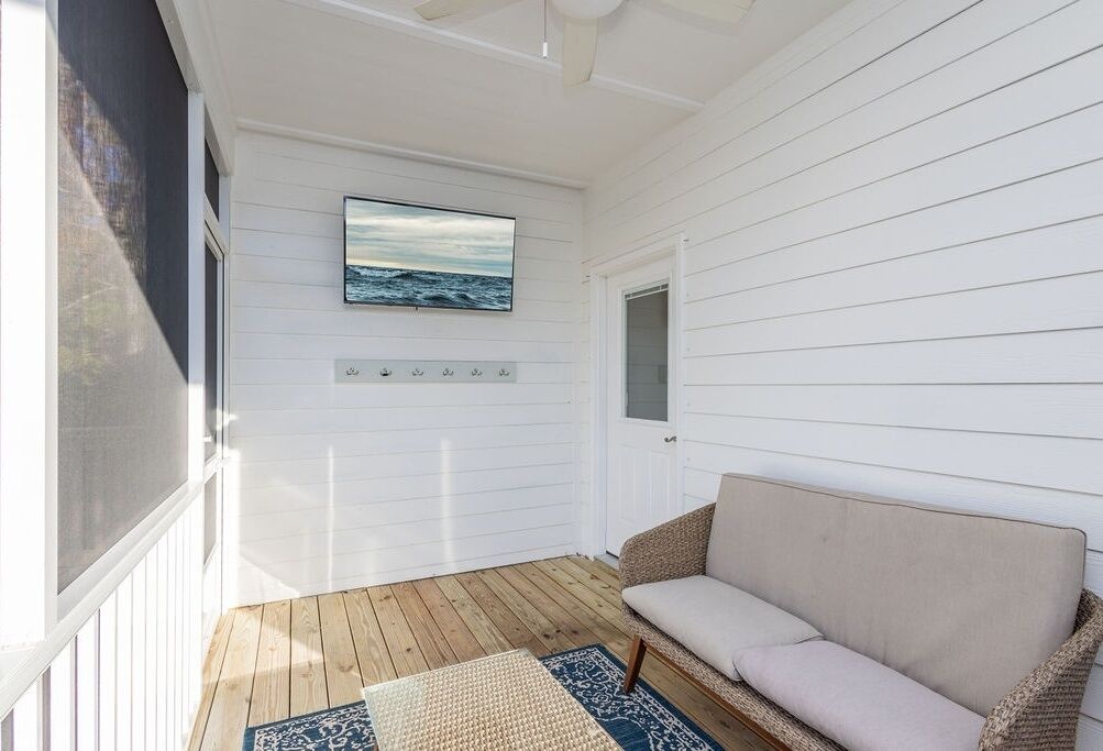 Une véranda avec un canapé beige, un plancher en bois et un tableau encadré représentant l’océan.