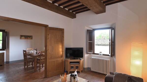 Una sala de estar con televisor, muebles de madera, un comedor y una ventana con vistas.