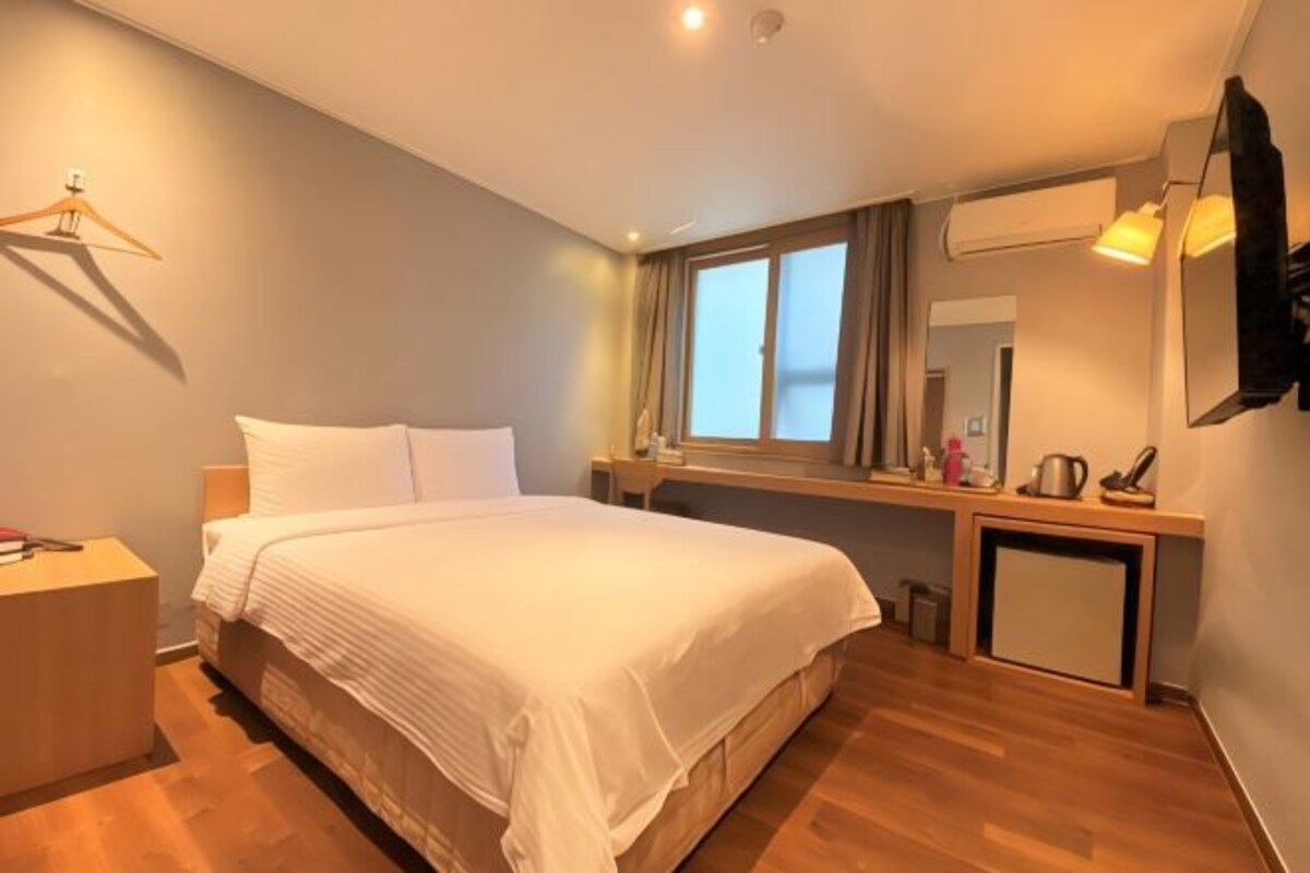 A hotel room with a bed, bedside table, dresser, mirror, and a window with curtains.
