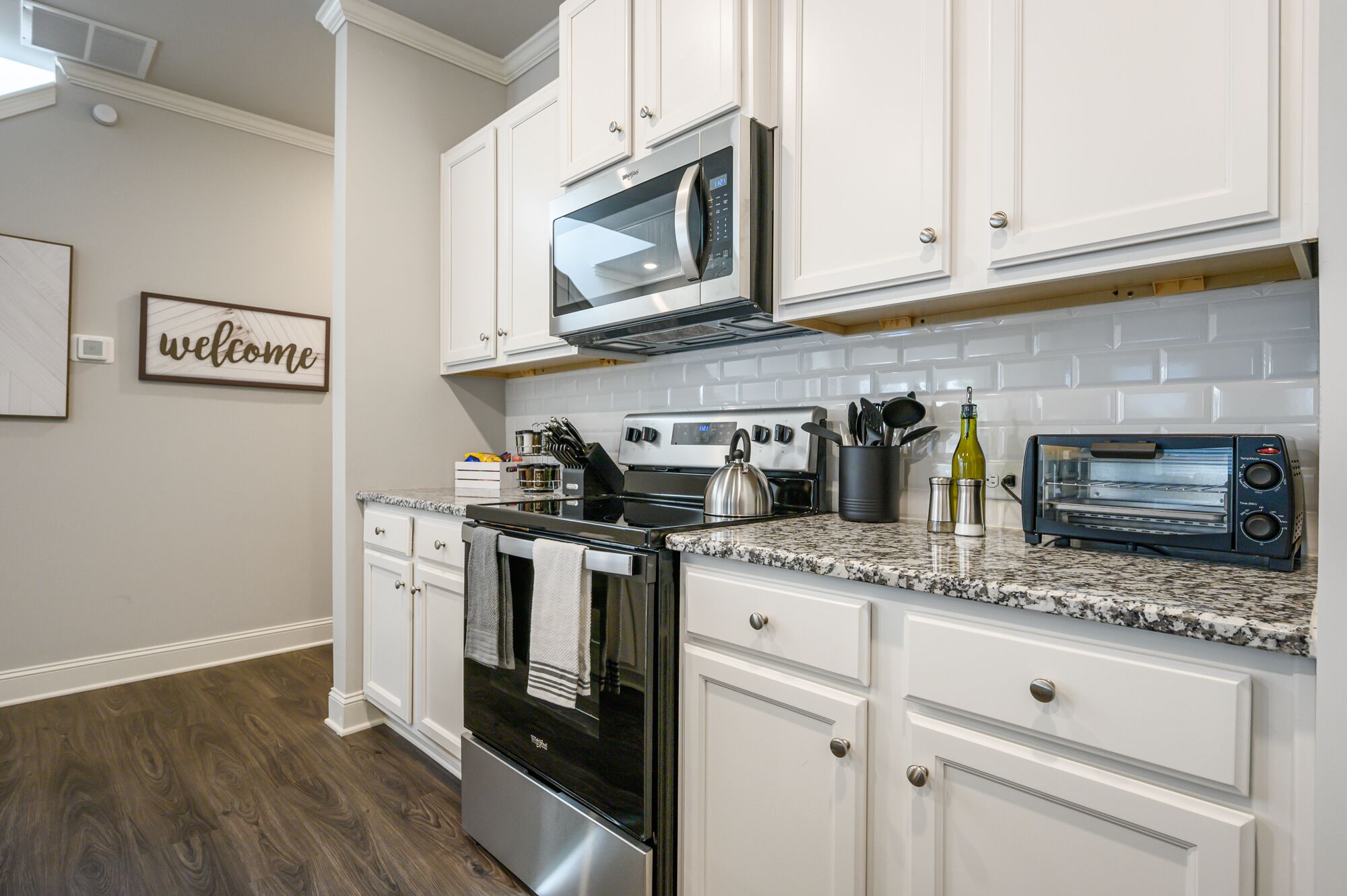 A modern kitchen with white cabinetry, a stainless steel stove, a microwave, and a toaster.
